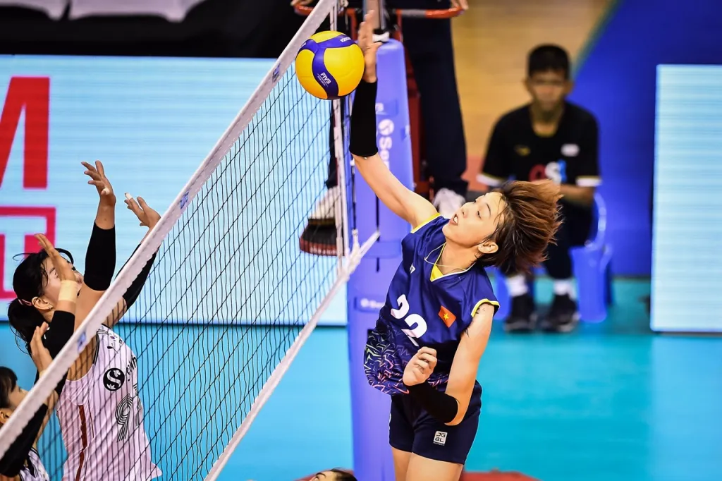 Vận động viên đang thi đấu bóng chuyền trong nhà, nơi chiều cao lưới bóng chuyền nam được áp dụng.